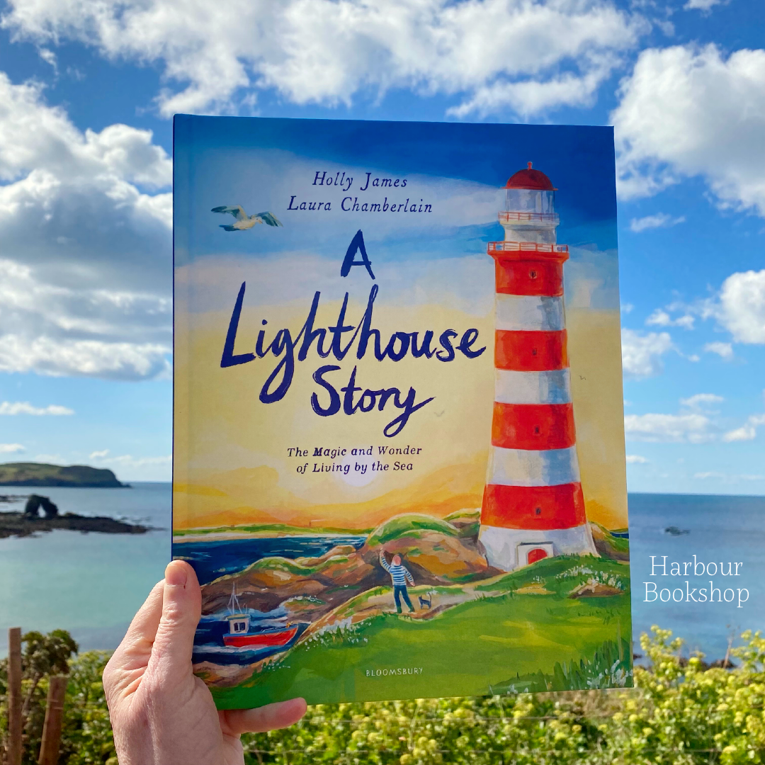 A Lighthouse Story by Holly James and Laura Chamberlain, held up against the South Devon coast outside the Harbour Bookshop