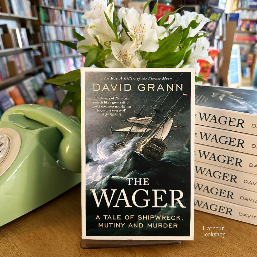 David Grann's The Wager hardback styled on a vintage sage-green rotary telephone with white alstroemeria flowers, on display inside the Harbour Bookshop